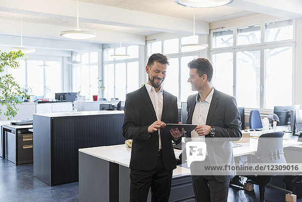 Two businessmen standing in office  discussing solutions  using digital tablet