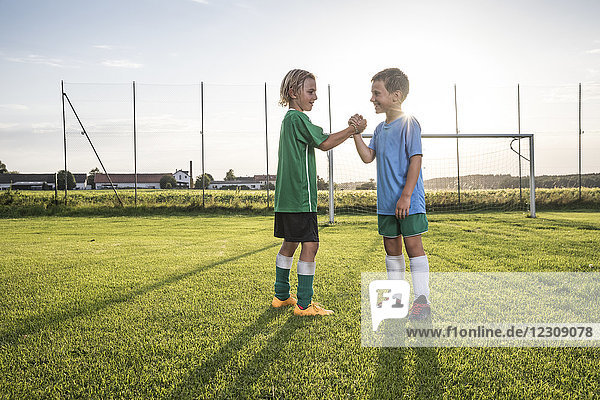 Lächelnde junge Fußballspieler beim Händeschütteln auf dem Fußballplatz