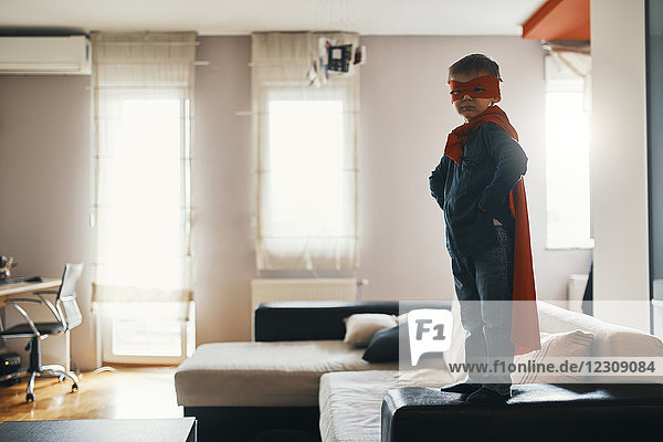 Kleiner Junge verkleidet als Superheld auf dem Wohnzimmertisch stehend.