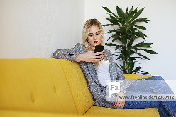 Geschäftsfrau auf gelber Couch sitzend  mit Smartphone