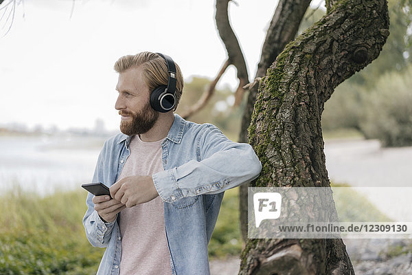 Deutschland  Düsseldorf  Mann mit Smartphone und Kopfhörer beim Musikhören im Freien