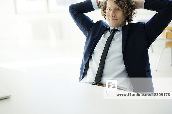 Entspannter Geschäftsmann sitzt im Büro mit den Händen hinter dem Kopf