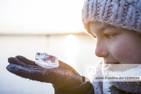 Deutschland  Brandenburg  Straussee  Porträt eines Mädchens  das auf dem zugefrorenen See steht und ein Stück Eis auf der Hand sieht