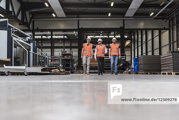 Three men wearing hard hats and safety vests walking on factory shop floor
