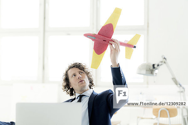 Geschäftsmann sitzt in seinem Büro und spielt mit einem Spielzeugflugzeug.