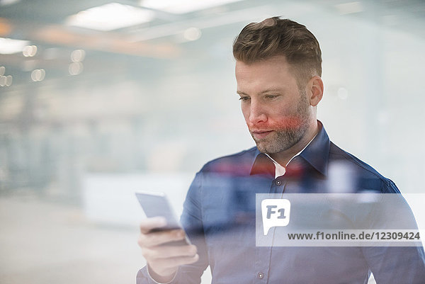 Businessman looking on cell phone behind glass pane