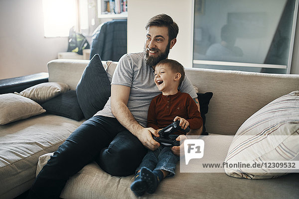 Glücklicher Vater und Sohn sitzen zusammen auf der Couch und spielen Computerspiel