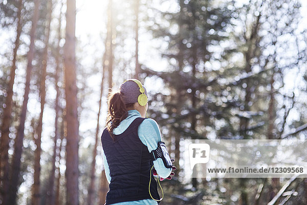 Rückansicht des jungen Joggers mit Kopfhörer im Wald bei einer Pause