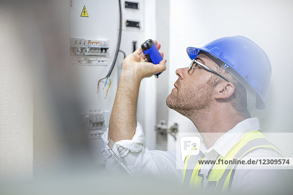 Electrician with flashlight at fusebox