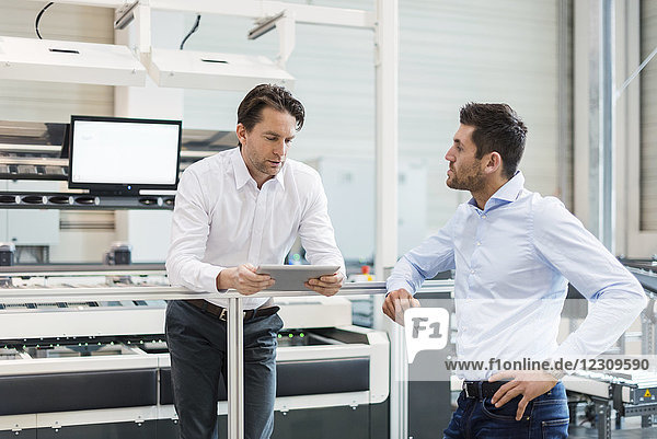 Two businessmen with tablet talking in modern factory