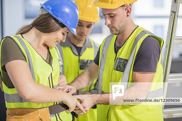 Construction worker helping colleague with tool belt