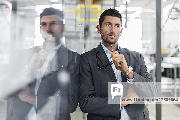 Businessman leaning against glass pane in modern factory thinking