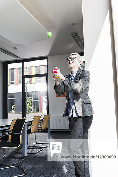 Lachende Geschäftsfrau jongliert mit Bällen im Büro