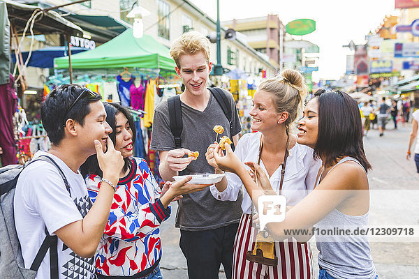 Thailand  Bangkok  Khao San Road  Gruppe von Freunden  die auf dem Straßenmarkt lokale Speisen kosten