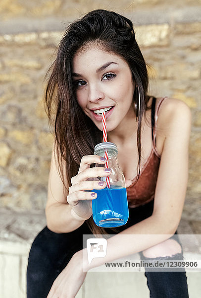 Porträt einer lächelnden brünetten Frau beim Trinken von blauer Limonade