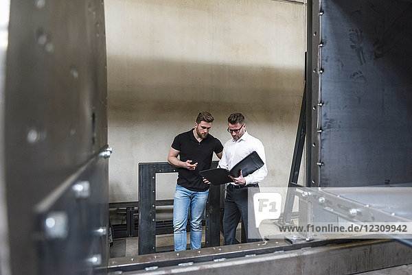Two men with folder talking on factory shop floor