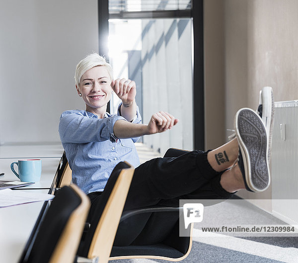 Portrait of happy woman stretching on chair in office