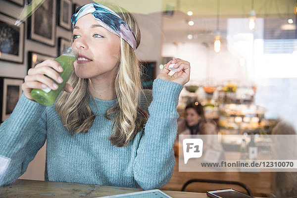 Junge Frau trinkt Gemüsesaft am Fensterplatz eines Cafés