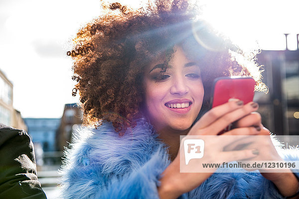 Portrait of woman with afro looking at smartphone smiling