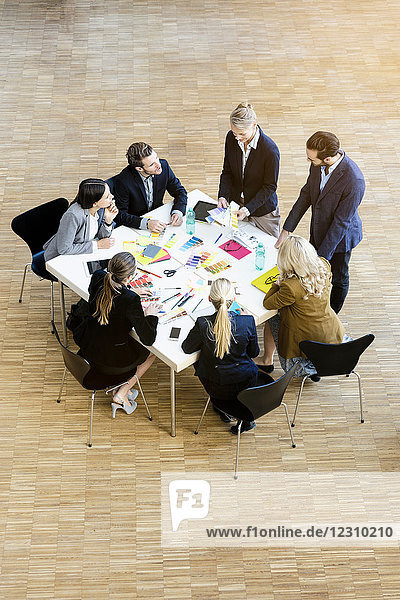 Businesswomen and men in office atrium discussing design swatches on table  high angle view