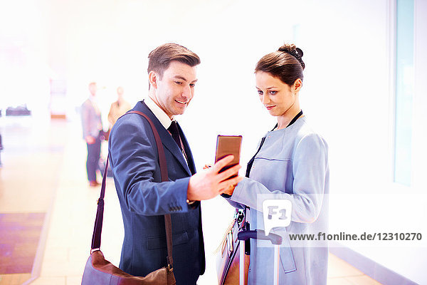 Young businesswoman and man in airport looking at smartphone