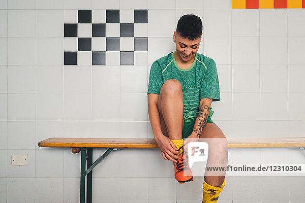 Fussballspieler bindet Schnürsenkel auf der Bank in der Umkleidekabine