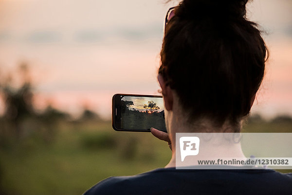 Junge Frau fotografiert mit einem Smartphone im Okavango-Delta  Rückansicht  Botswana  Afrika