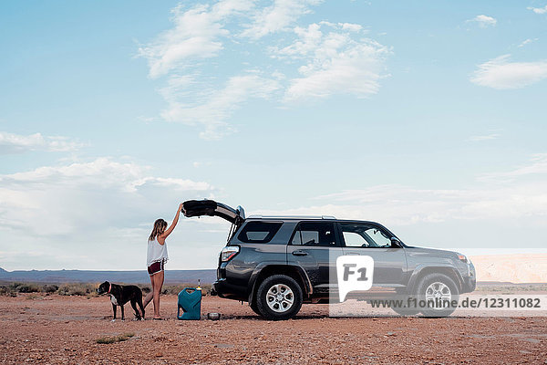 Young woman in remote setting  opening boot of SUV  dog beside her  Mexican Hat  Utah  USA