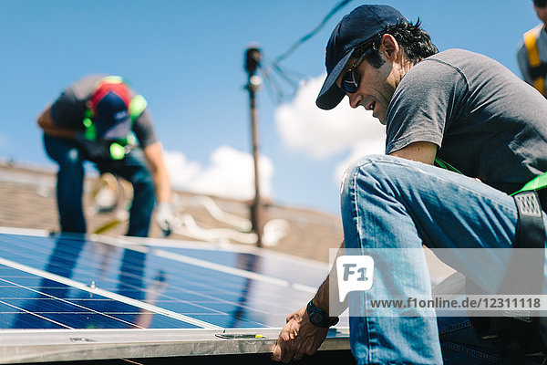 Drei Handwerker installieren Sonnenkollektoren auf dem Hausdach  Blickwinkel gering