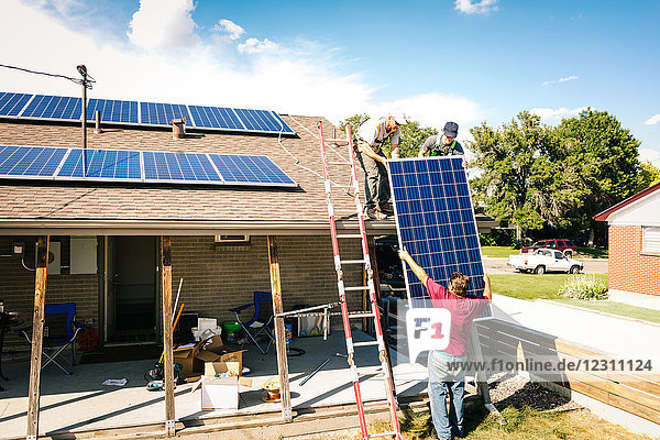 Handwerker heben Sonnenkollektoren auf das Hausdach und bereiten die Installation vor