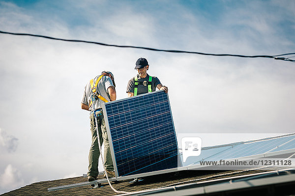 Zwei Handwerker installieren Sonnenkollektoren auf dem Hausdach  Blickwinkel gering