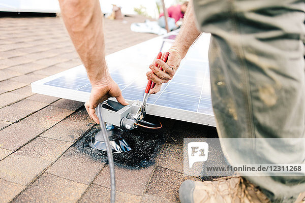 Handwerker bei der Installation von Sonnenkollektoren auf dem Hausdach  Mittelteil  Nahaufnahme