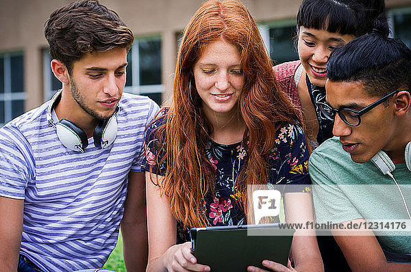 Gruppe von College-Studenten  die gemeinsam im Freien ein digitales Tablet betrachten