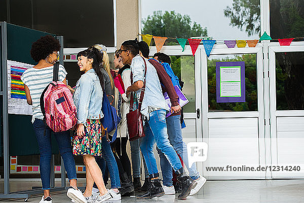 College students eagerly looking at bulletin board outside building on campus