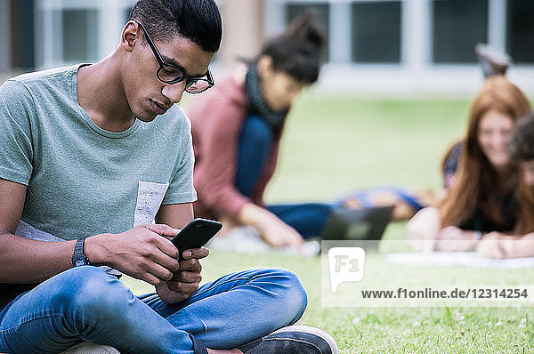 Männlicher Student  der sein Smartphone im Freien benutzt