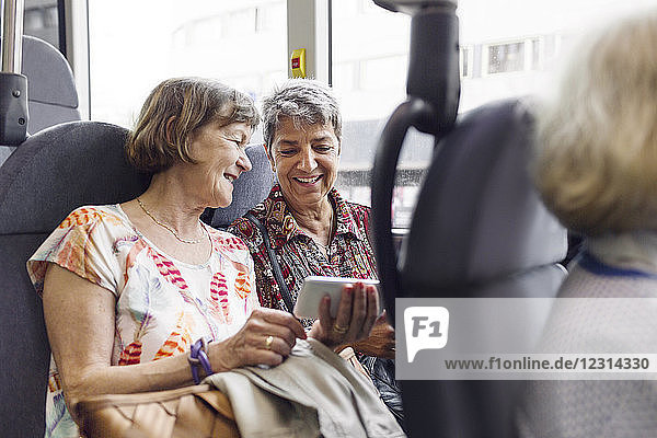 Zwei lächelnde Frauen schauen im Bus auf ihr Handy