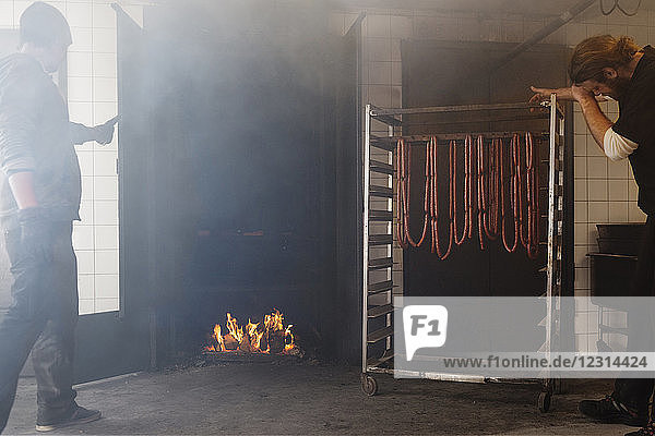 Two men inserting pork sausages into smokehouse