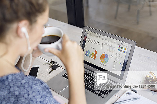Woman drinking coffee and looking at charts in laptop