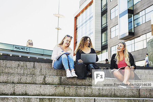Drei junge Frauen mit Laptop  auf Stufen sitzend