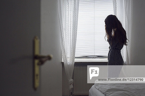 Nachdenkliche junge Frau am Fenster stehend