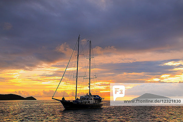 Silhouettiertes touristisches Segelboot bei Sonnenaufgang vor Anker in der Nähe der Insel Chinese Hat im Galapagos-Nationalpark  Ecuador  Südamerika