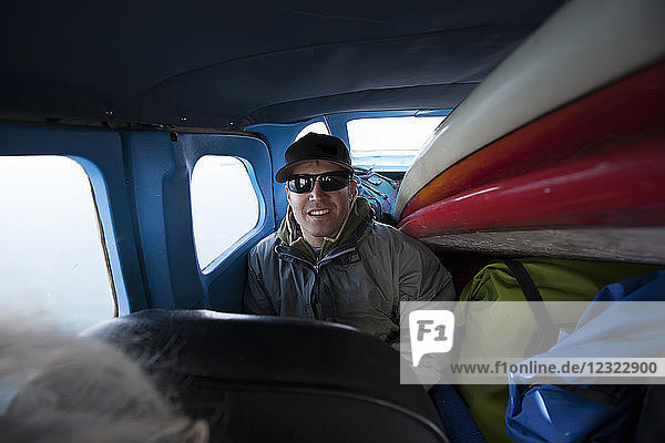 Ein Surfer sitzt auf dem Rücksitz eines Buschflugzeugs  das mit Vorräten und Surfbrettern beladen ist; Alaska  Vereinigte Staaten von Amerika