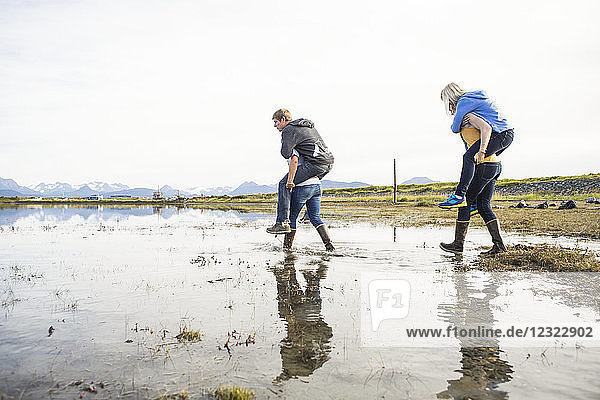 Freunde in Gummistiefeln  die Freunde durch eine nasse Küstengegend tragen  Süd-Zentral-Alaska; Homer  Alaska  Vereinigte Staaten von Amerika