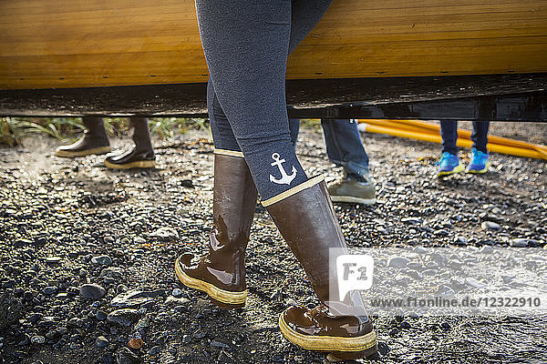 Close up of woman walking in rubber boots carrying a wooden boat  South-central Alaska; Homer  Alaska  United States of America