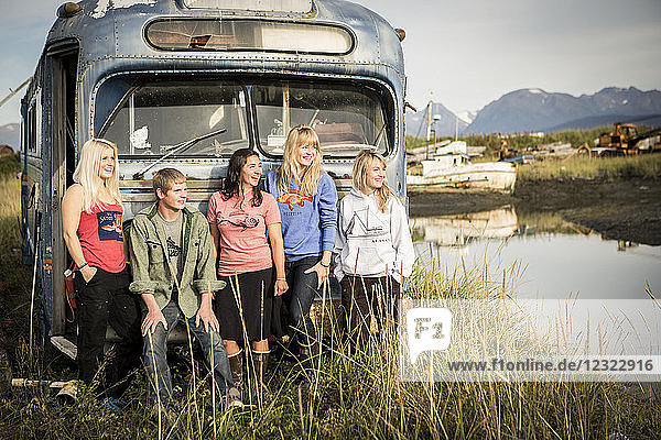 Group of young adults hanging out at a vintage rundown bus along coastal Homer  South-central Alaska; Homer  Alaska  United States of America