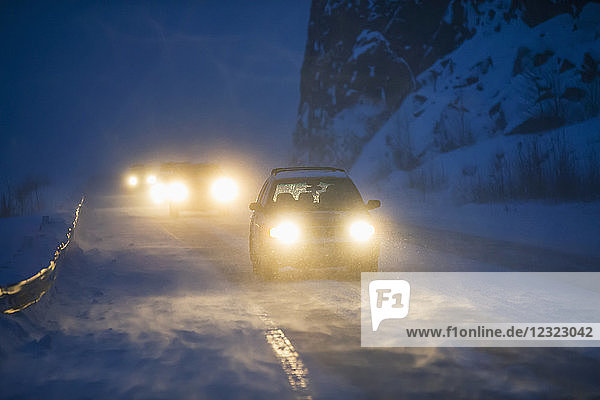 Car headlights from traffic illuminate the blowing snow on the Seward Highway during a dark winter night Kenai Peninsula Turnagain Arm South-central Alaska; Alaska United States of America