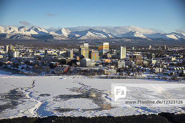 Aerial view of snow covering the the sea ice on the frozen shores of downtown Anchorage  the Chugach Mountains in the background beyond the office buildings and hotels in downtown Anchorage in winter  South-central Alaska; Anchorage  Alaska  United States of America