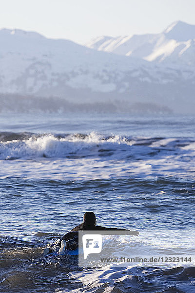 Female surfer enters the waters of Kachemak Bay  South-central Alaska; Homer  Alaska  United States of America