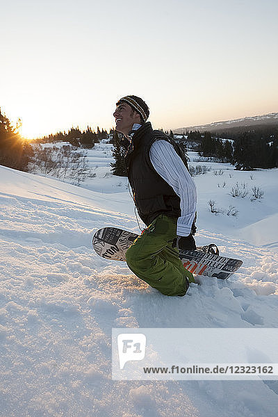 Mann  der bei Sonnenuntergang mit einem Snowboard bergauf geht  in der Nähe von Homer  Süd-Zentral-Alaska; Alaska  Vereinigte Staaten von Amerika