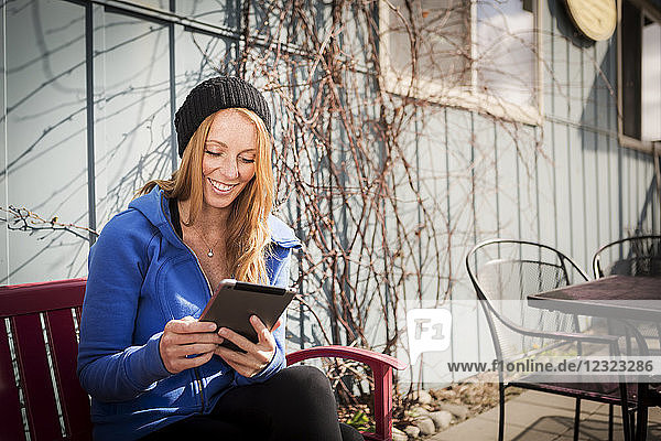 Junge Frau sitzt mit ihrem Tablet vor einem Geschäft in der Innenstadt von Anchorage  South-central Alaska; Anchorage  Alaska  Vereinigte Staaten von Amerika